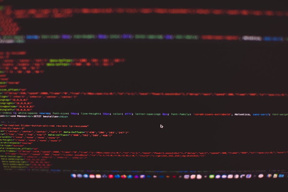 Close-up view of a laptop screen displaying colorful lines of code in a darkened environment, highlighting a programming interface typically associated with software development and technical work, wi